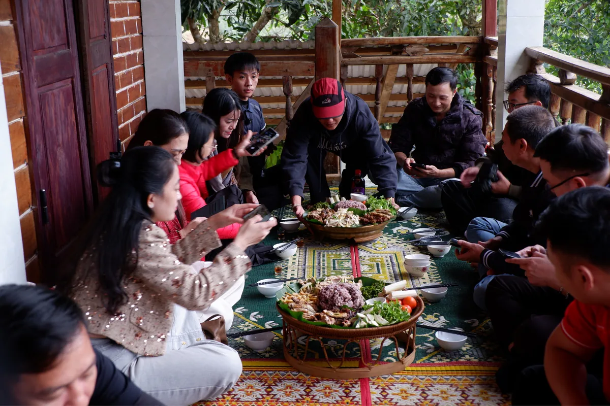 Mọi người quây quần thưởng thức bữa ăn với các món ăn bày trên mâm tại nhà sàn